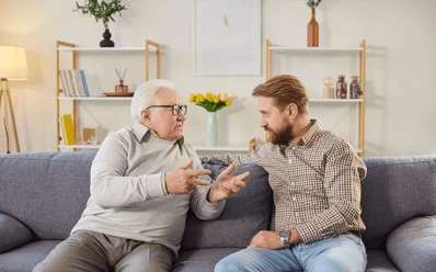 Padre conversa con su hijo adulto en la sala de una vivienda