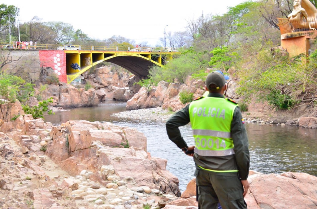 Un policía colombiano con chaleco reflectivo observa el río Guatapurí y el puente amarillo en el balneario Hurtado de Valledupar, zona acordonada por la investigación contra alias el Feo.