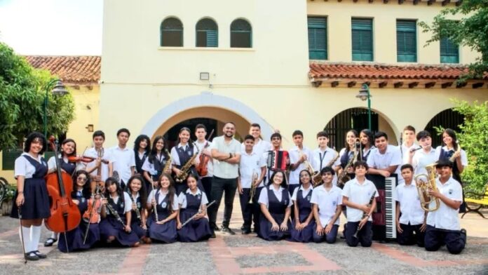 Foto grupal de los estudiantes de la Banda Sinfónica de la Institución Educativa Loperena en Valledupar, posando con sus instrumentos tras el lanzamiento de su versión de 'Olvídala' para el Festival Vallenato.