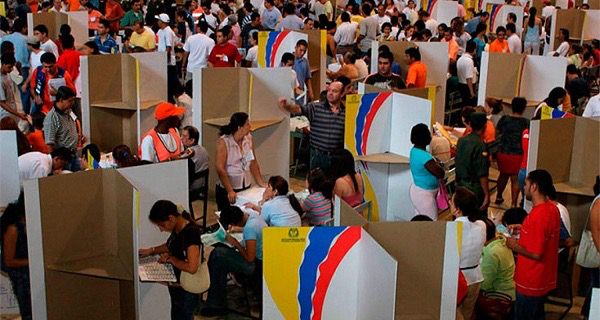 Puesto de votación concurrido en Colombia con ciudadanos en cubículos de cartón de la Registraduría durante jornada electoral.