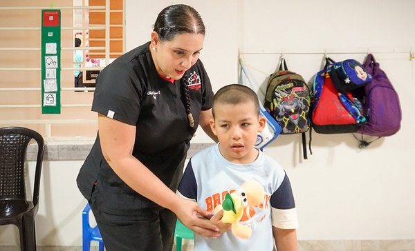 Maestra consuela a un niño llorando con las manos en el rostro en un aula, representando la crisis de atención para niños con autismo en Valledupar.