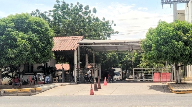 Vista de la portería o entrada principal a la urbanización OGB en Valledupar, con dos portones metálicos cerrados bajo un techo de zinc y tejas de barro. Se observan árboles, cables eléctricos y conos de señalización naranjas en la calle, reflejando el bloqueo preventivo ante la llegada de Afinia en Valledupar.