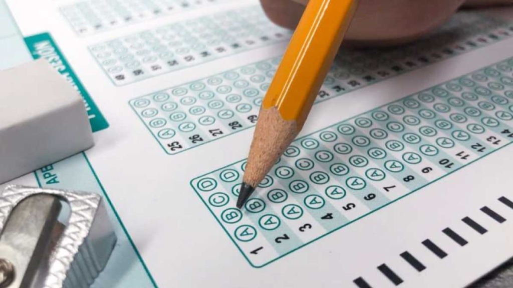 Primer plano de una mano rellenando con lápiz los círculos de la hoja de respuestas tipo Icfes durante las Pruebas Saber Pro y TyT, con borrador y sacapuntas visibles.
