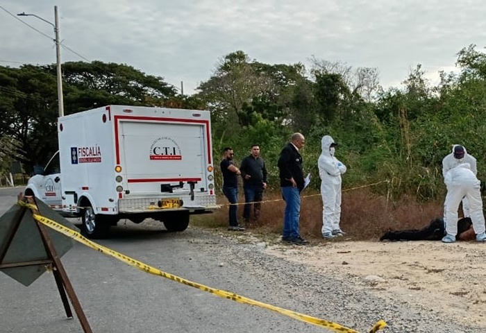 Escena judicial de levantamiento de cadáver tras uno de los homicidios en Valledupar. Se observa una camioneta blanca de criminalística del CTI de la Fiscalía General de la Nación. Expertos forenses con trajes blancos de bioseguridad inspeccionan un cuerpo en una zona de maleza, rodeados por cinta de seguridad amarilla.