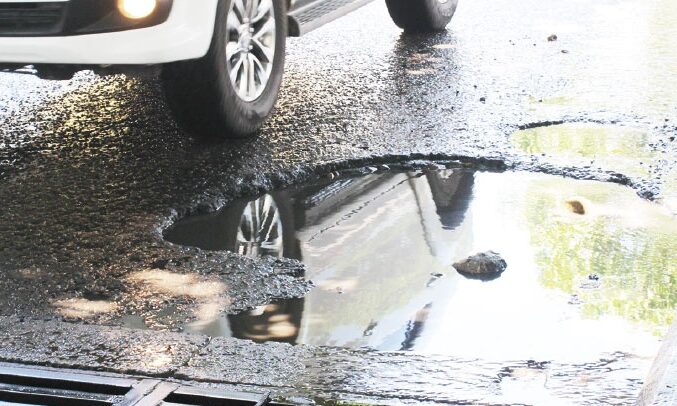 Fotografía de un hueco grande y profundo lleno de agua en una calle pavimentada de Valledupar, junto a una rejilla de alcantarillado metálica y un andén de baldosas deteriorado, con un vehículo blanco pasando en el fondo. Representa una queja ciudadana recurrente.