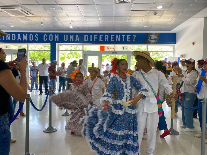 Pareja de niños bailando piloneras en el aeropuerto Alfonso López para recibir a los turistas que llegan en los vuelos al Festival Vallenato. De fondo se observa personal de logística y viajeros.