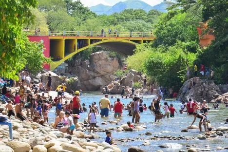Vista panorámica del Balneario Hurtado Valledupar en el río Guatapurí, mostrando el puente de colores (amarillo y rojo), bañistas en el agua y las rocas características rodeadas de vegetación. Representa el potencial turístico del sector.