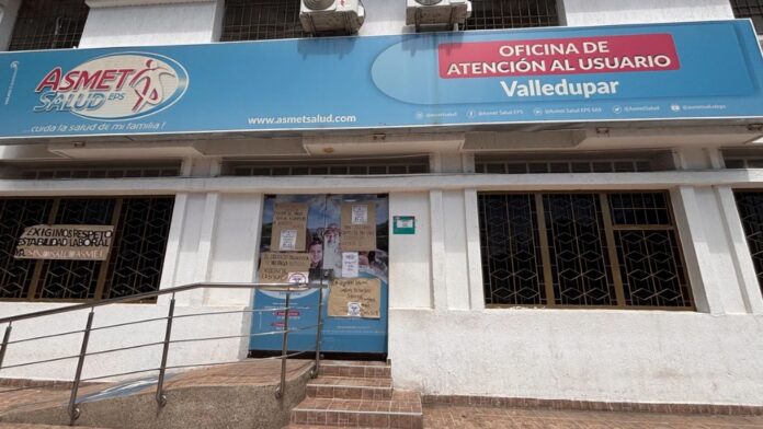 Fachada de la oficina de atención al usuario de Asmet Salud en Valledupar con carteles de protesta por salarios atrasados.