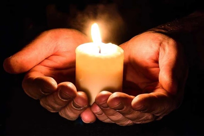Manos sosteniendo una vela encendida en la oscuridad durante la Vigilia Pascual.