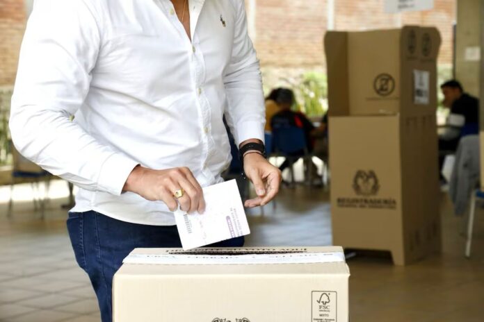 Primer plano de un ciudadano depositando su voto en la urna sellada de la Registraduría Nacional durante las elecciones presidenciales.