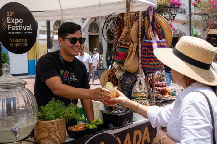 Joven emprendedor sirviendo una bebida refrescante a una turista en los stands de Expofestival en el Festival Vallenato 2026.