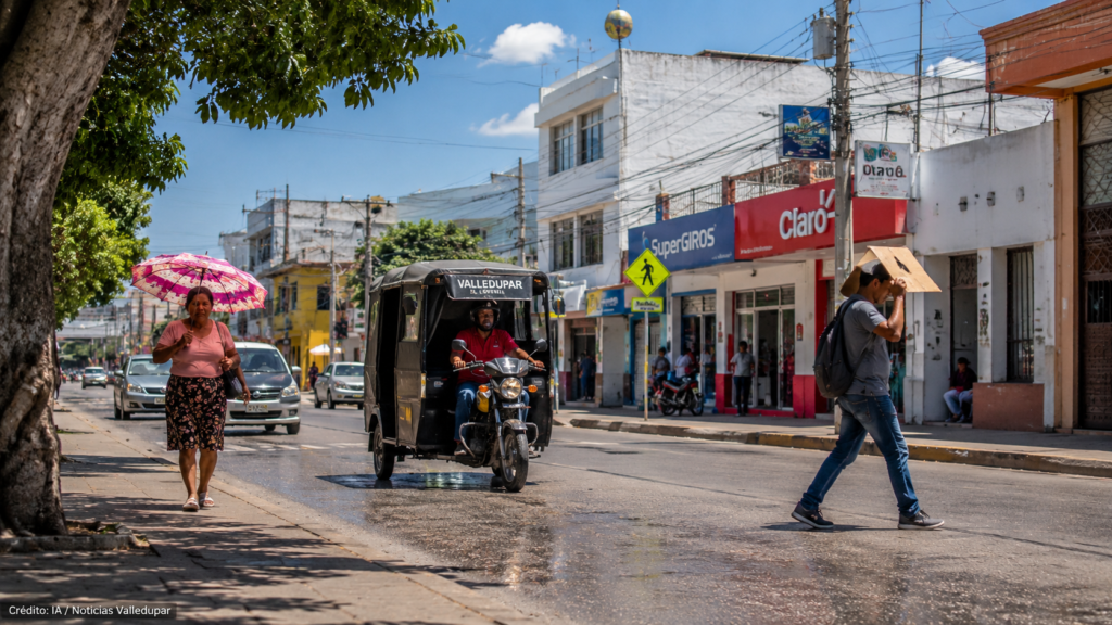 Calle de Valledupar bajo fuerte sol con mototaxi, peatones y personas protegiéndose del calor.